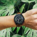 Man's wrist wearing a stylish watch in front of lush green foliage showcasing nature.